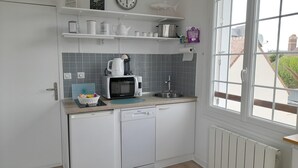 Una cocina compacta con microondas, hervidor y lavamanos. Hay repisas sobre la encimera con diversos objetos.