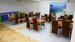 Un espace repas avec plusieurs tables et chaises, une vue sur la mer par une grande fenêtre et un sol carrelé.