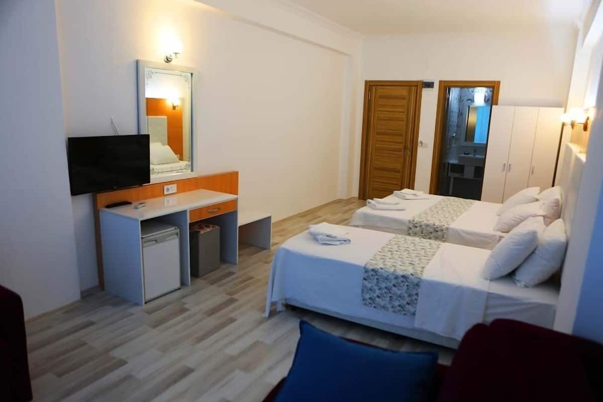A hotel room with a bed, a desk with a television, a wardrobe, and a mirror.