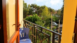 Un balcon avec une chaise bleue, une rambarde en métal et une vue sur des arbres et des voitures garées.