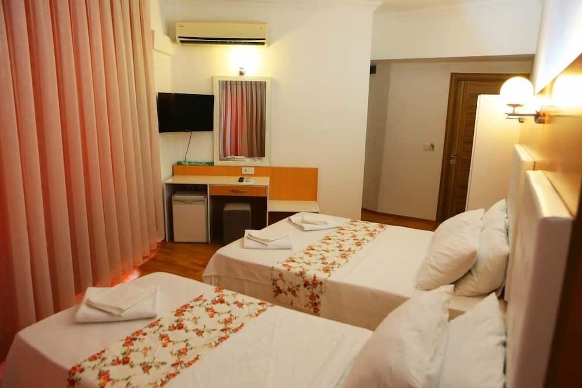 A hotel room with two beds, a desk, a television, and an air conditioning unit.