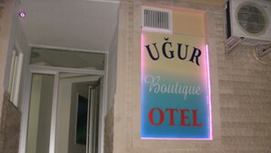 Une enseigne indiquant « UGUR Boutique Hotel », avec une porte d’entrée bien visible et un appareil de climatisation fixé au mur.