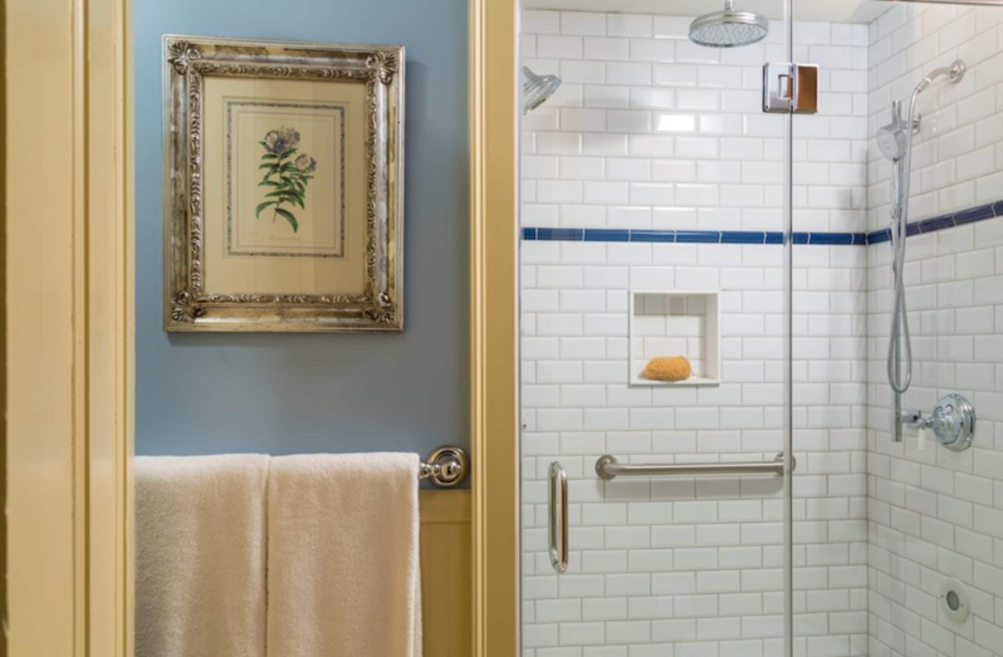 Une salle de bain avec un tableau encadré au mur, un porte-serviettes et une douche aux carreaux blancs avec une bande bleue.