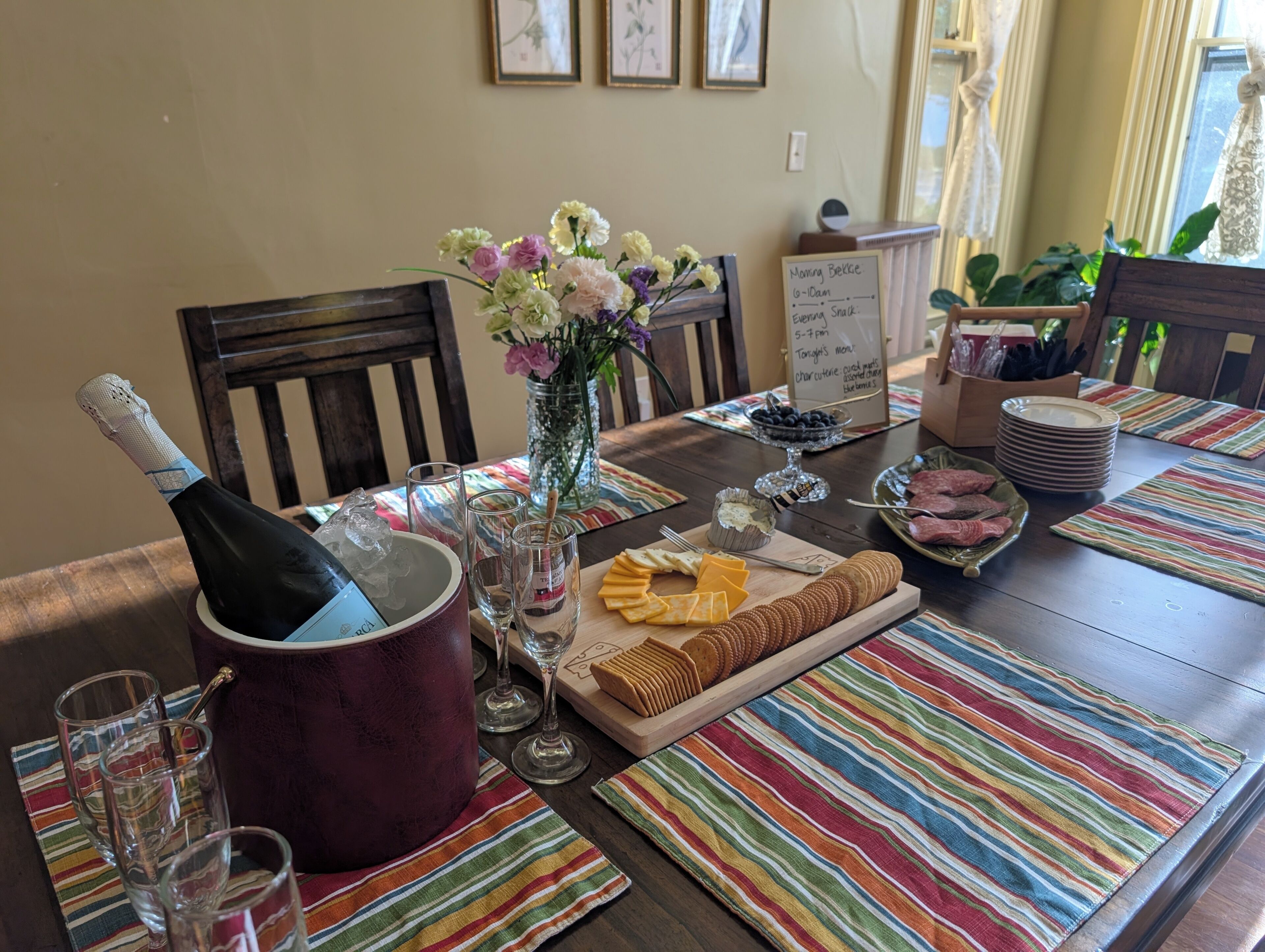 A dining table set with a bottle of champagne, glasses, a floral centerpiece, and various snacks.