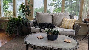 Et hyggeligt rum med en fletsofa, et rundt bord og potteplanter.