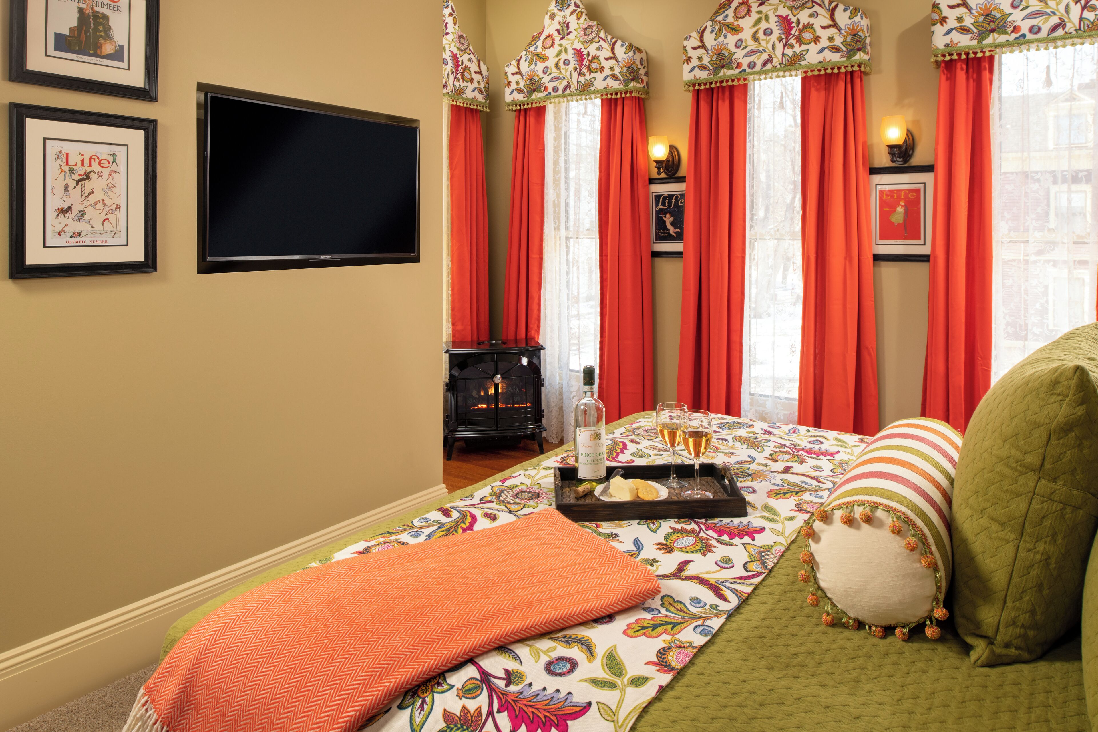 A hotel room with a bed, a flat-screen TV, a fireplace, and a tray with glasses and a bottle.