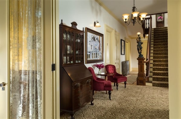 A hallway with a wooden cabinet, two red armchairs, a table with flowers, and a staircase with a railing.