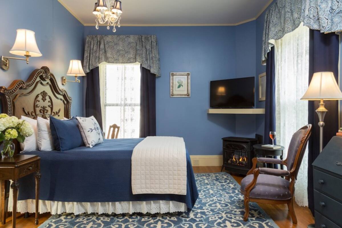 A bedroom with a large bed, a television, a fireplace, and a chair.