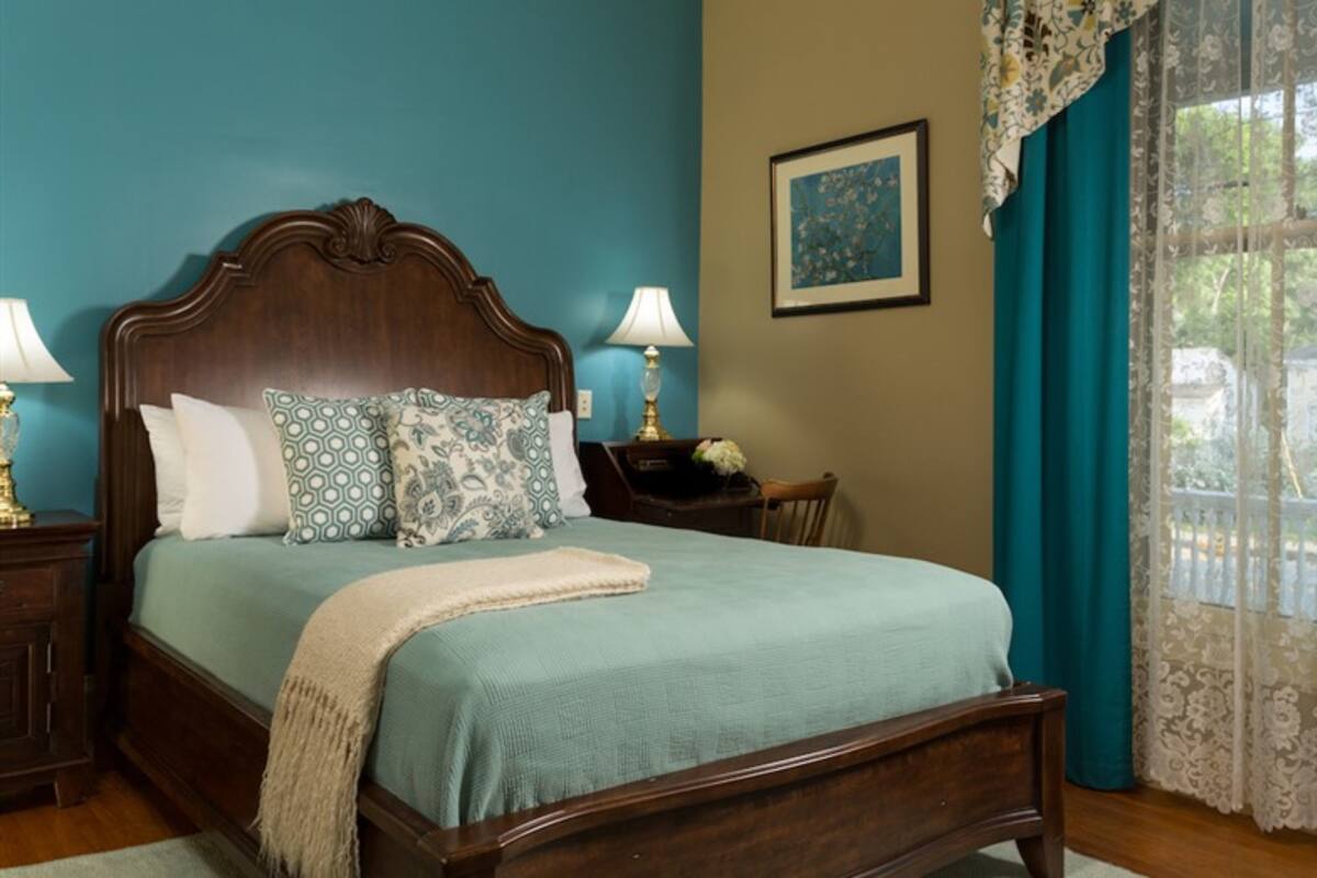 A neatly made bed with a wooden headboard, two bedside tables with lamps, a framed picture on the wall, and a window with curtains.