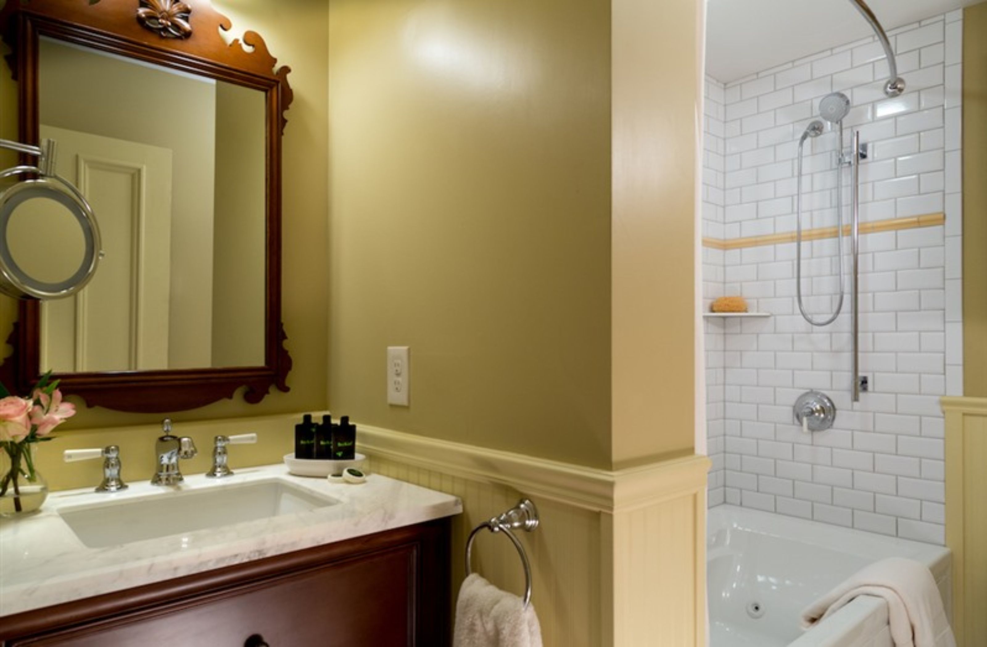 A bathroom with a double sink, a large mirror, and a shower area with a white tiled wall.