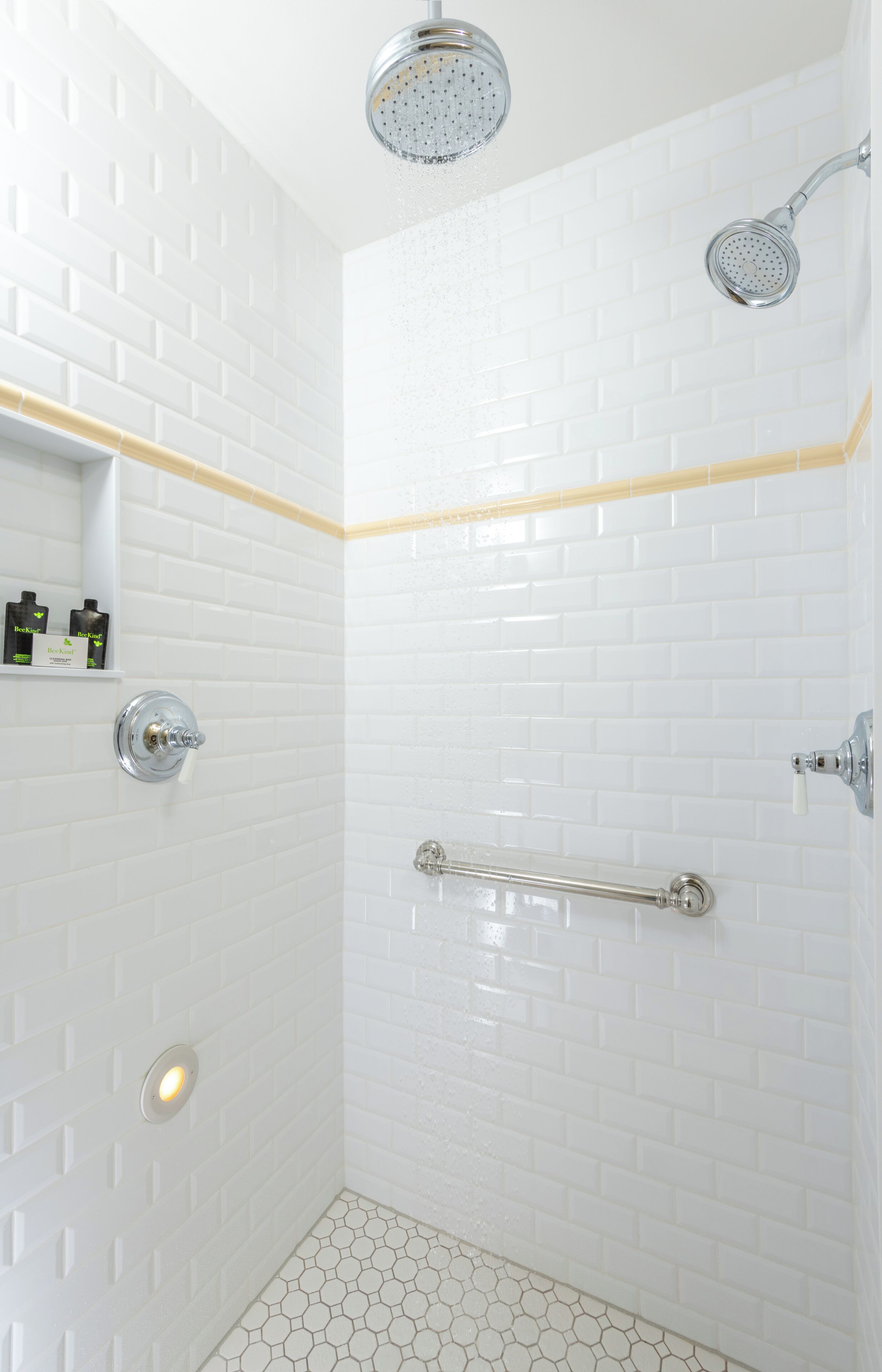 A shower with white subway tiles, a yellow accent strip, and a handrail.
