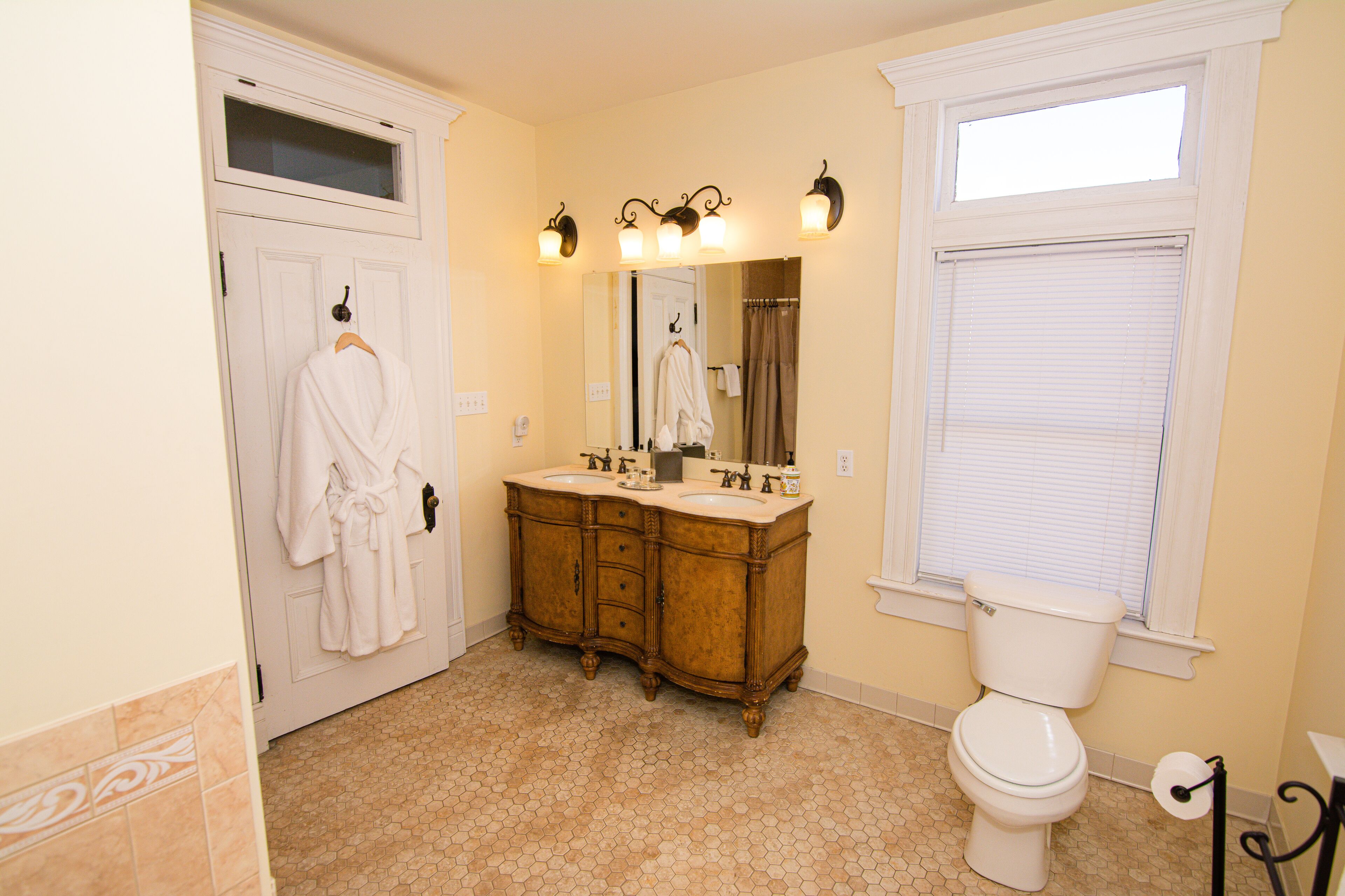 A bathroom with a double sink vanity, a toilet, and a window with blinds.