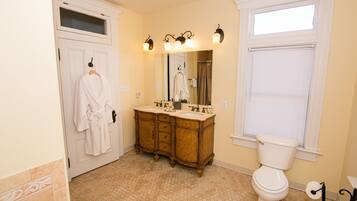 A bathroom with a double sink vanity, a toilet, and a window with blinds.