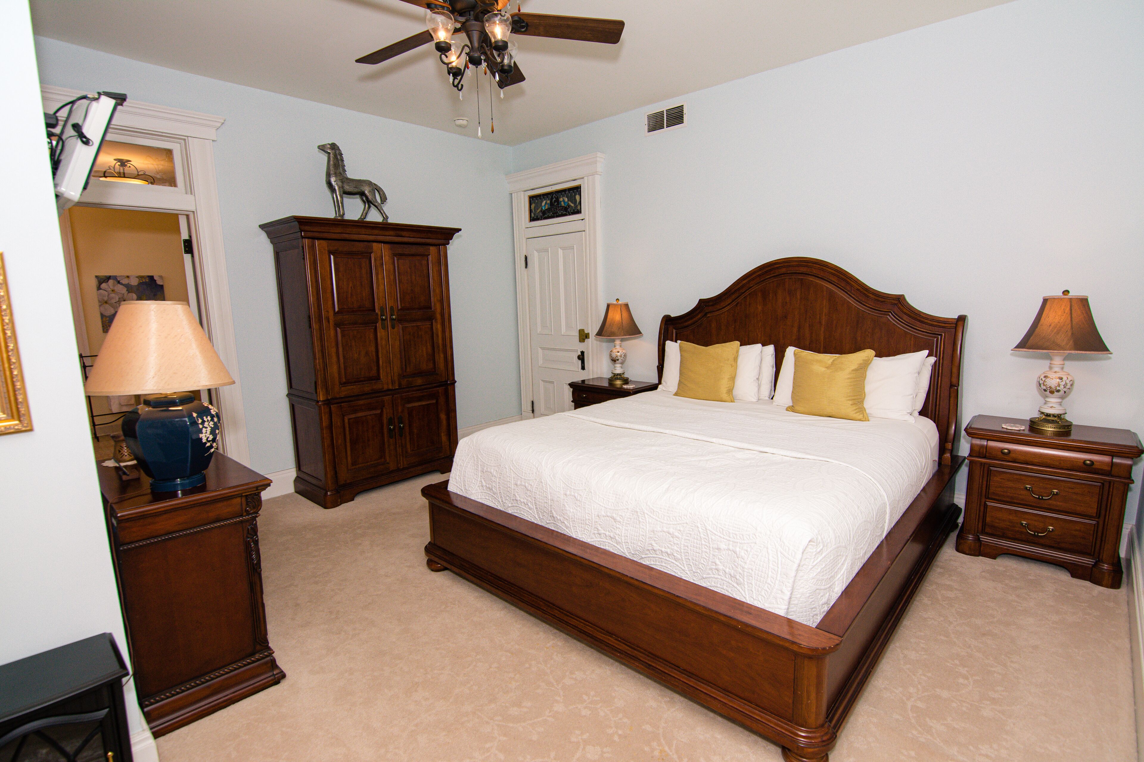 A bedroom with a large bed, wooden furniture, and a ceiling fan.
