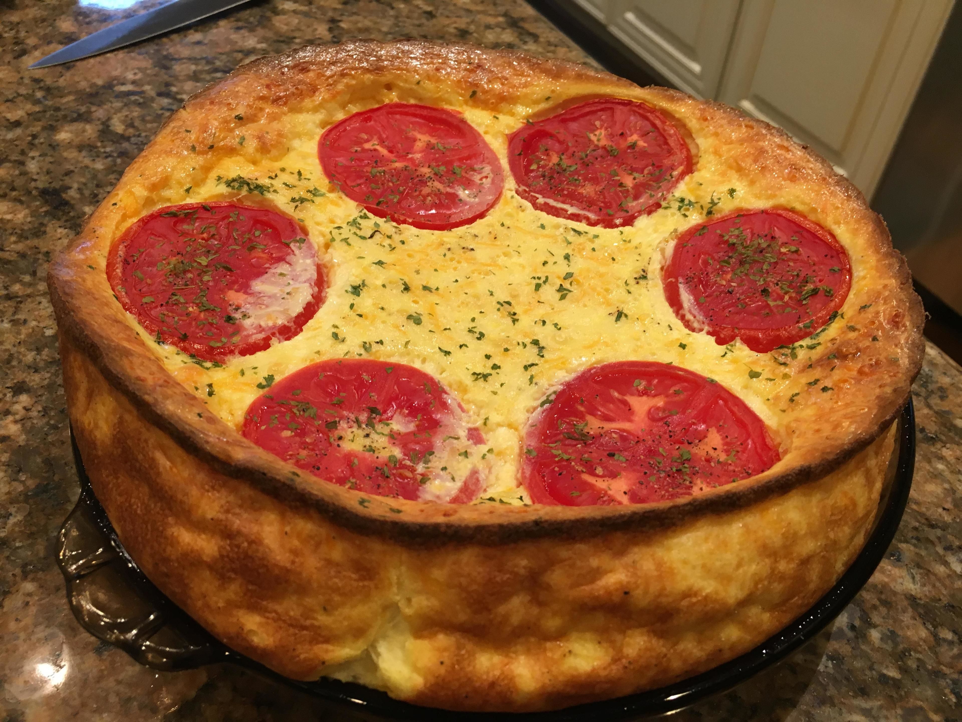 Una quiche redonda con rodajas de tomate y hierbas sobre un plato negro.