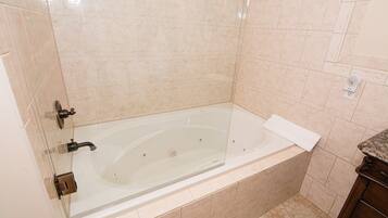 Un baño moderno con bañera de hidromasaje con mampara de vidrio, azulejos color beige y un mueble de tocador de madera.