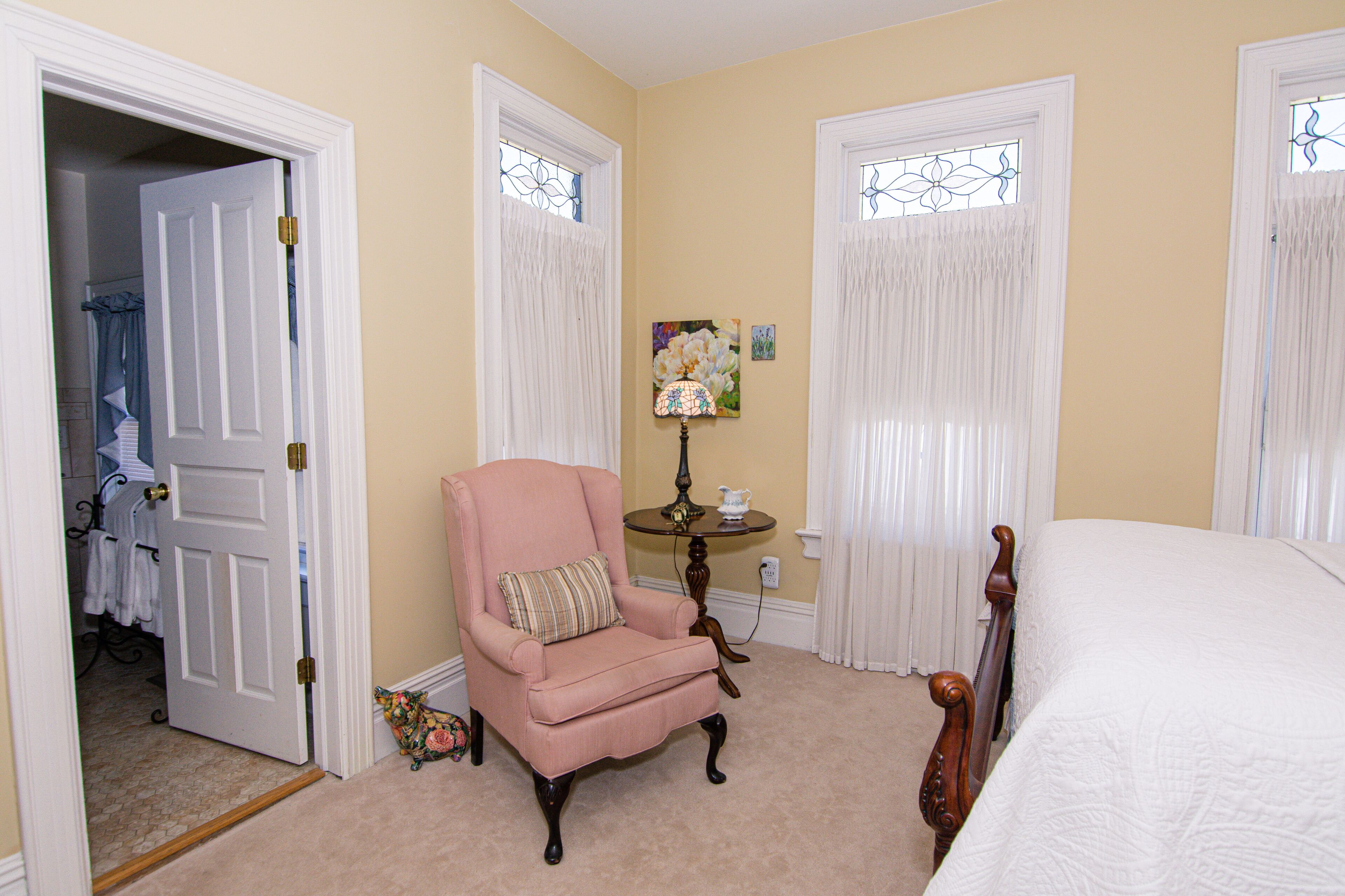 A bedroom with a bed, a chair, a lamp, and a door leading to a bathroom.