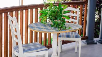 A round table with a checkered tablecloth, two white chairs with striped cushions, and a potted plant with green foliage.