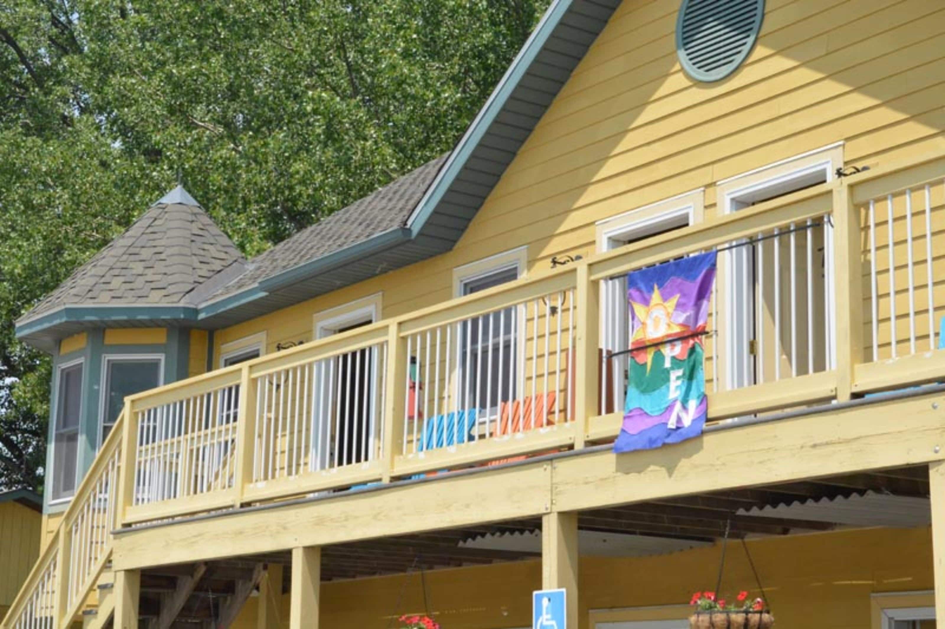 A yellow building with a balcony, a ramp, and a handicapped accessibility sign.