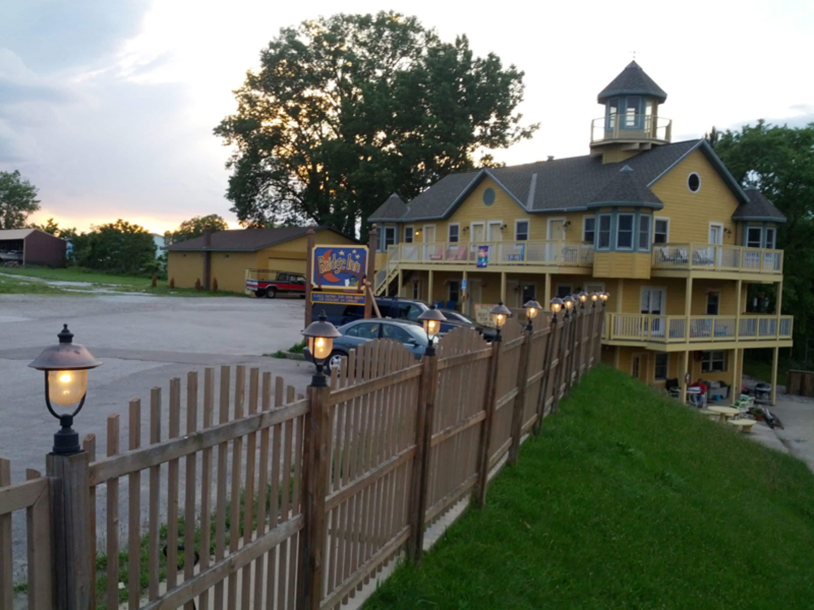 A yellow building with a sign for Bridge Inn, a fenced parking area, and a grassy area with picnic tables.