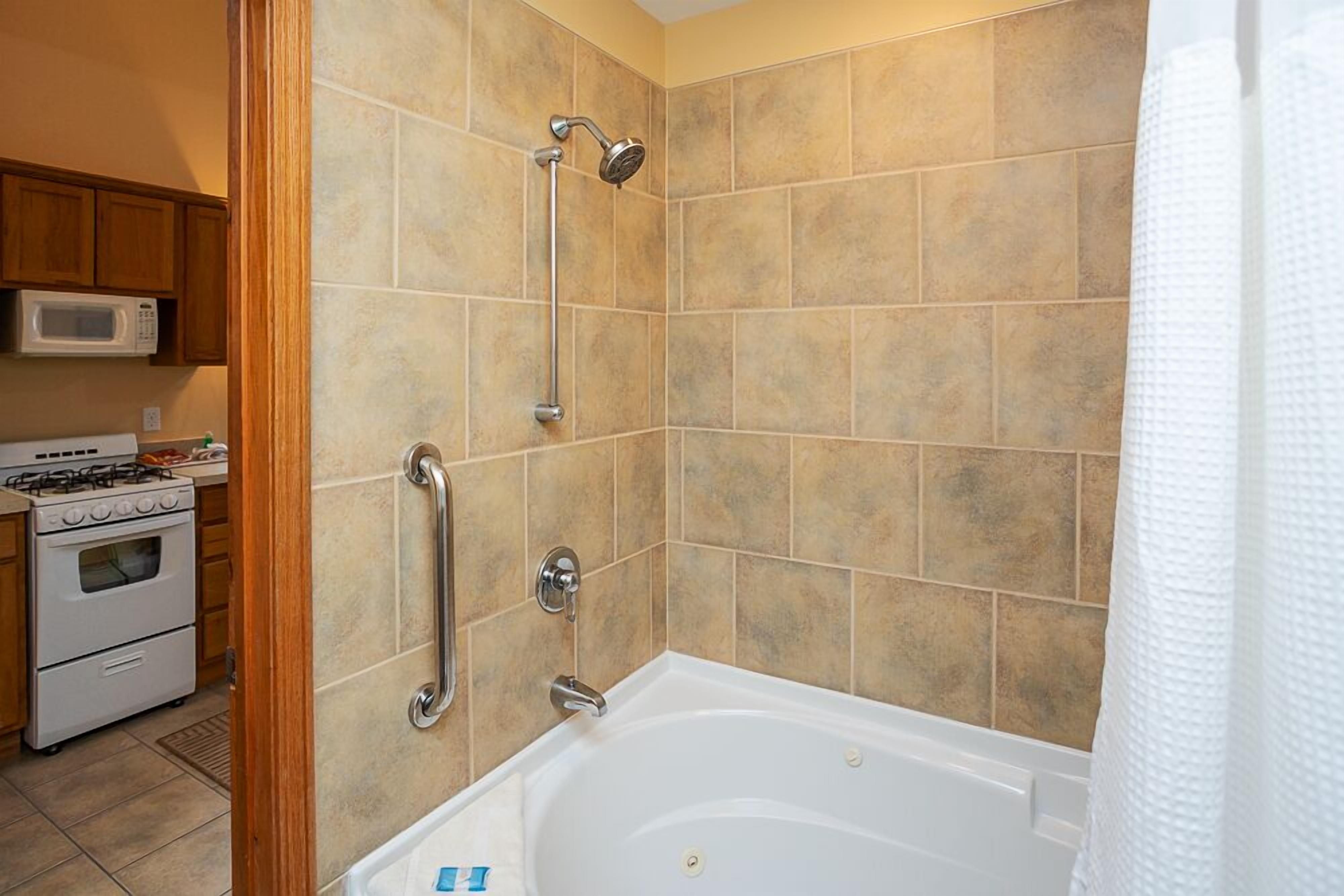 A bathroom with a bathtub, shower, and handrails.