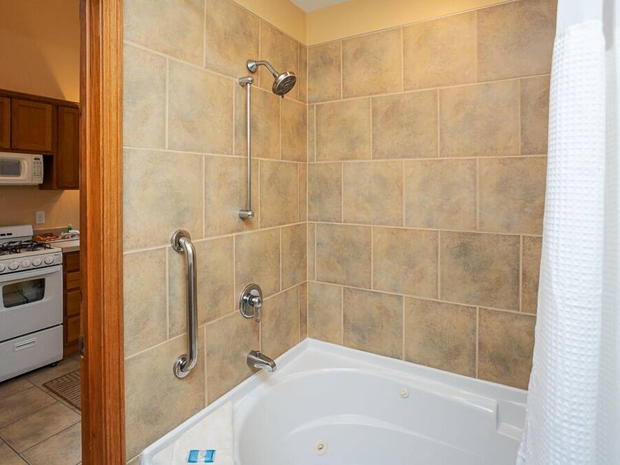 A bathroom with a bathtub, shower, and handrails.