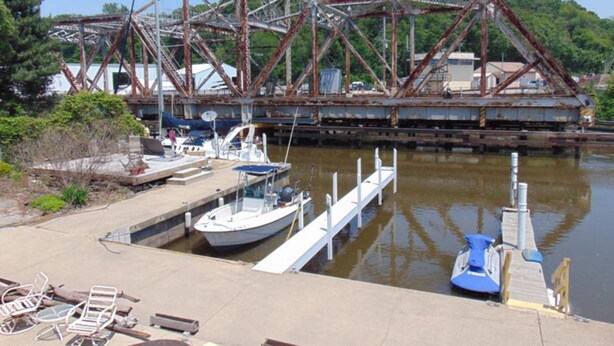 A dock with a boat, a rusty bridge, and greenery in the background. - Bridge Inn (Michigan City)