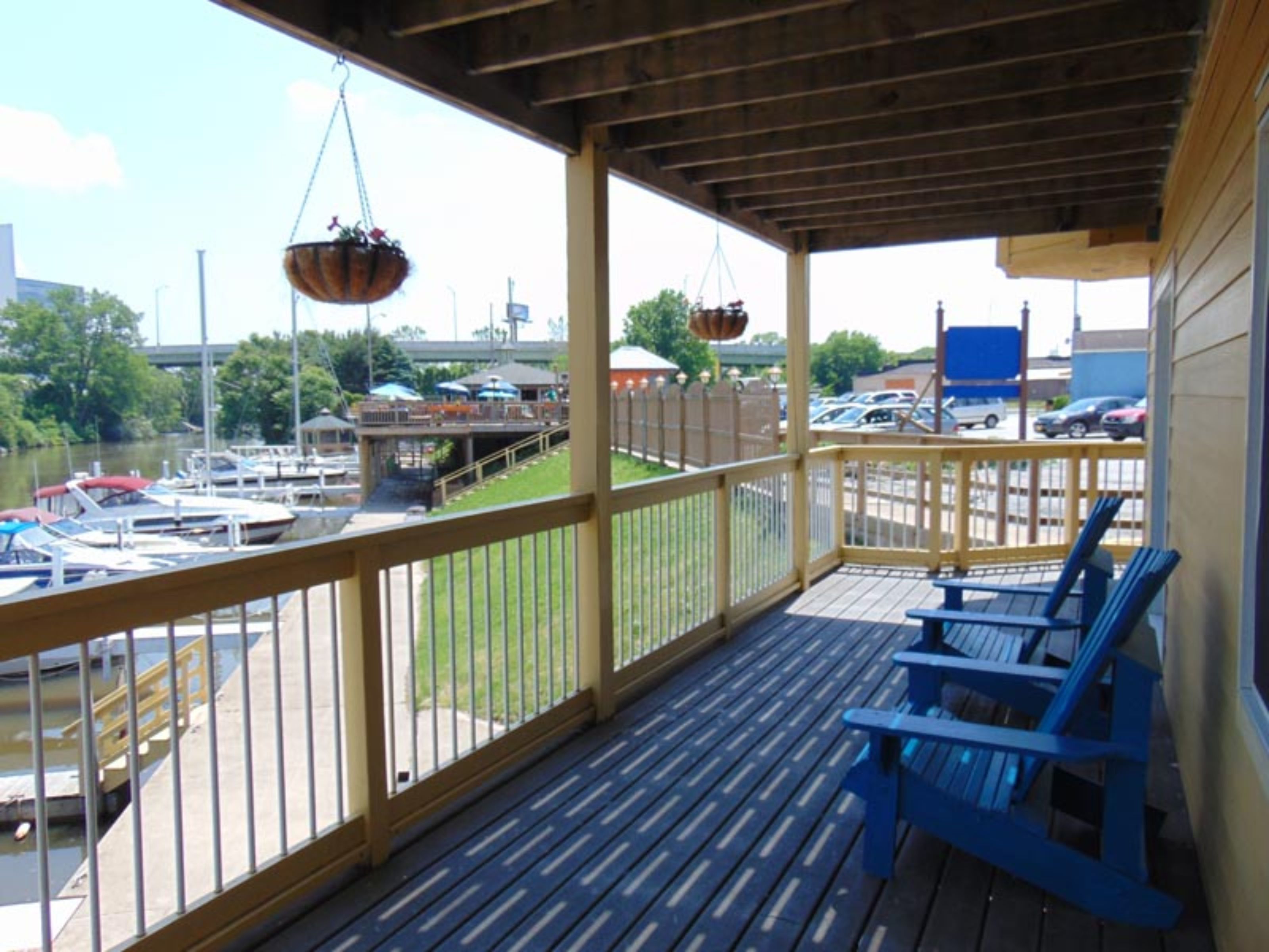 Una terraza techada al aire libre con sillas azules, una maceta colgante y vistas a un puerto deportivo con barcos.