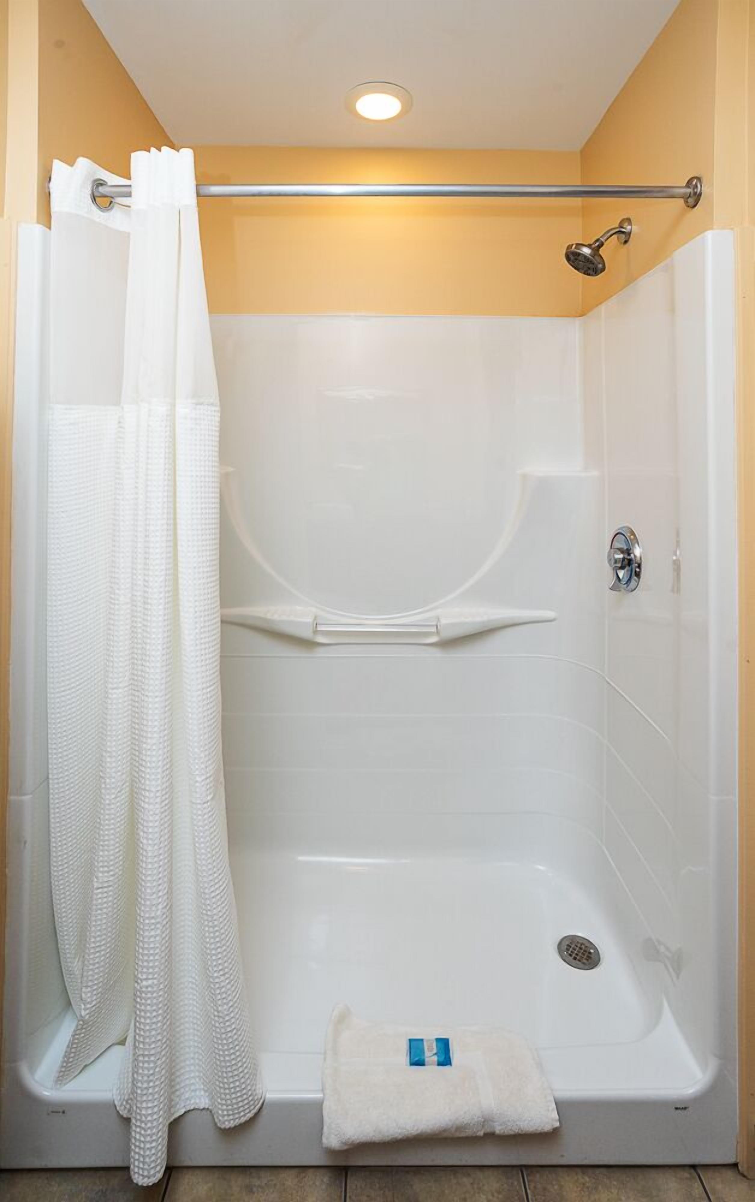A walk-in shower with a white tiled wall, a shower curtain, a towel, and a handheld showerhead.