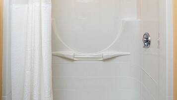 A walk-in shower with a white tiled wall, a shower curtain, a towel, and a handheld showerhead.
