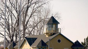 A multi-story yellow building with a tower, balconies, and a dock area. - Bridge Inn (Michigan City)