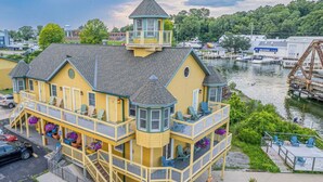 A multi-story yellow building with a turret and balcony, located near a body of water with boats and a dock. - Bridge Inn (Michigan City)