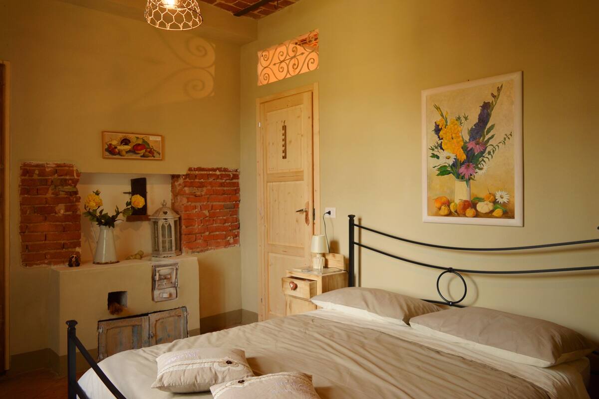 Un dormitorio con cama, mesita de noche, lámpara, cómoda, pared de ladrillo y un cuadro con flores.