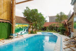 Une piscine ornée d’une fresque représentant une cascade, entourée de verdure et de structures en bambou.