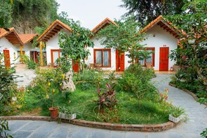 Une rangée de bâtiments blancs aux portes rouges et aux toits de tuiles, entourés de jardins luxuriants et bordés d’un sentier en pierre.