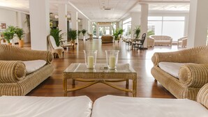 Un hall espacioso con sofás de mimbre, una mesa de centro de cristal con velas y plantas en macetas.