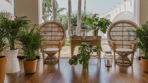 Una habitación con sillas de mimbre, plantas en macetas y vista a palmeras desde afuera.
