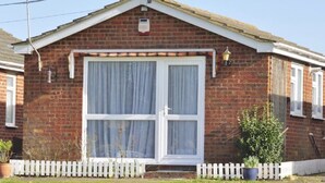 A brick house with a white-framed window, a white picket fence, and a small garden area. - Leysdown Chalet 28 (Sheerness)