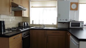 A kitchen with wooden cabinets, a gas stove, a sink, a microwave, and a clock on the wall. - Leysdown Chalet 28 (Sheerness)