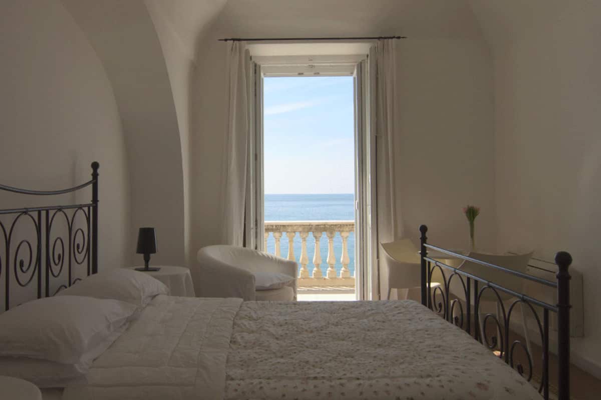 Une chambre avec un lit, une table de chevet, une chaise et une vue sur la mer depuis un balcon.