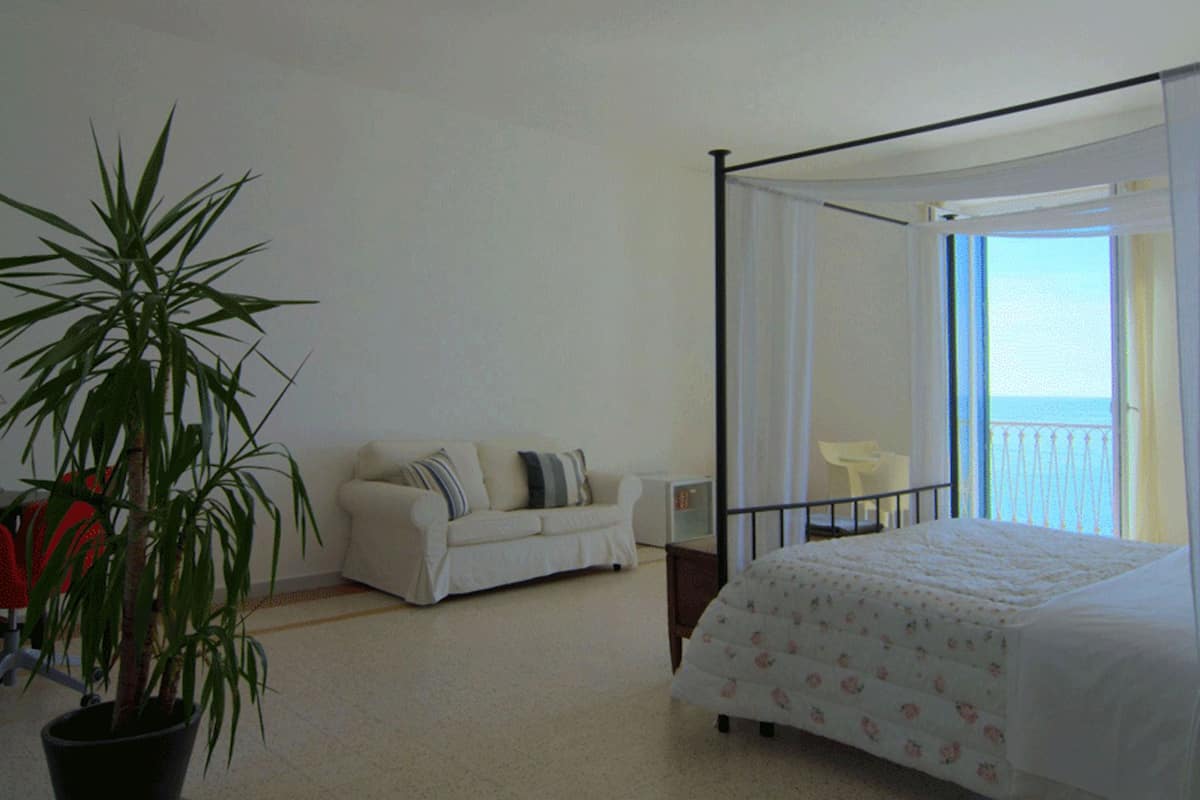 Une chambre à coucher avec un lit à baldaquin, une plante en pot, un canapé blanc et un balcon avec une chaise.
