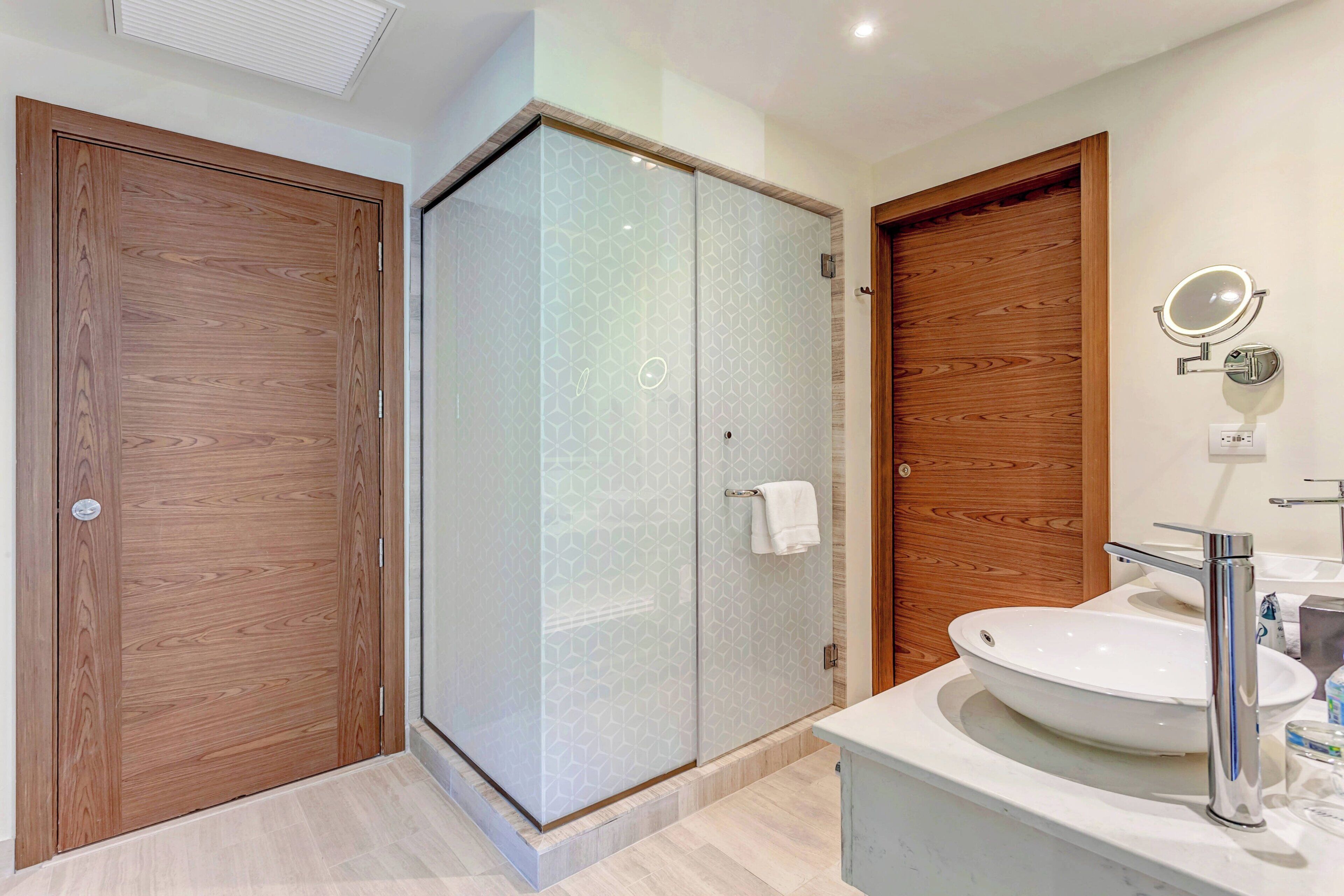 Un baño moderno con ducha de vidrio, puertas de madera y un lavamanos blanco con espejo.