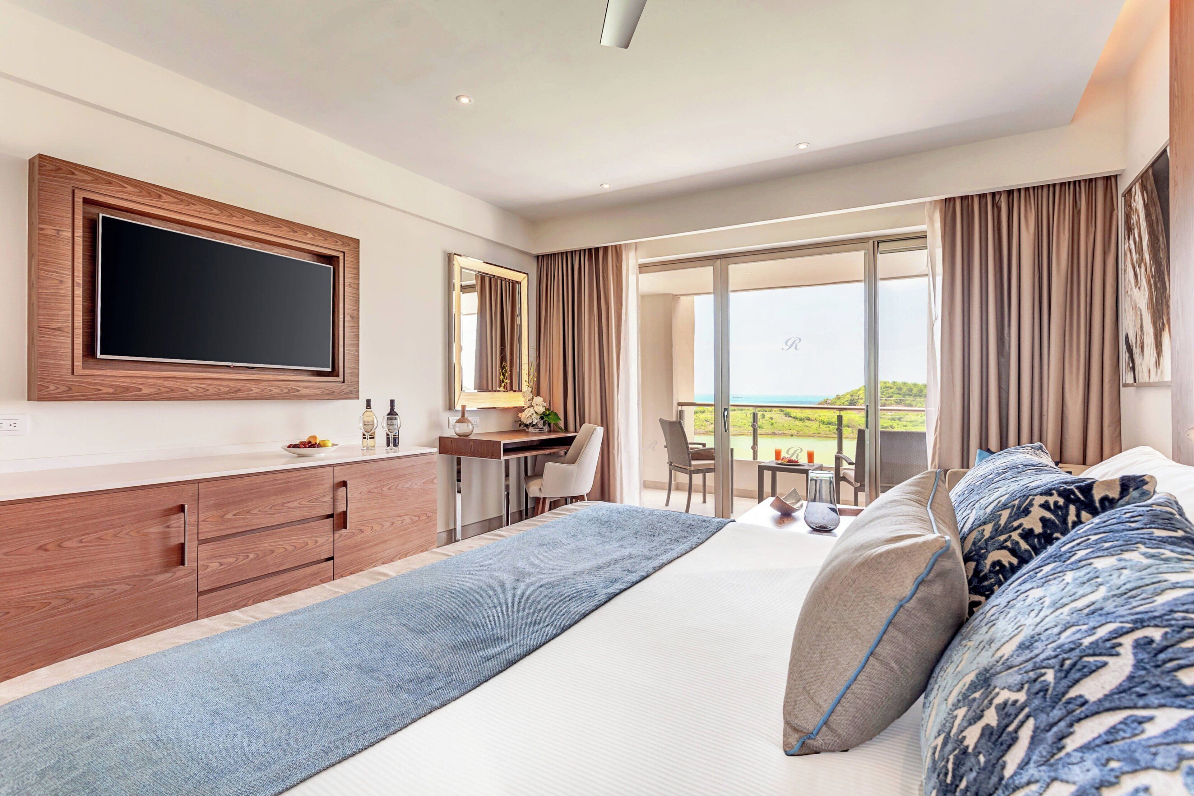 A modern hotel room with a large bed, a desk, a flat-screen TV, and a balcony with a view.