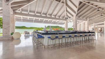 A spacious outdoor bar area with a long counter and multiple bar stools, a large round table, and a view of a natural landscape.