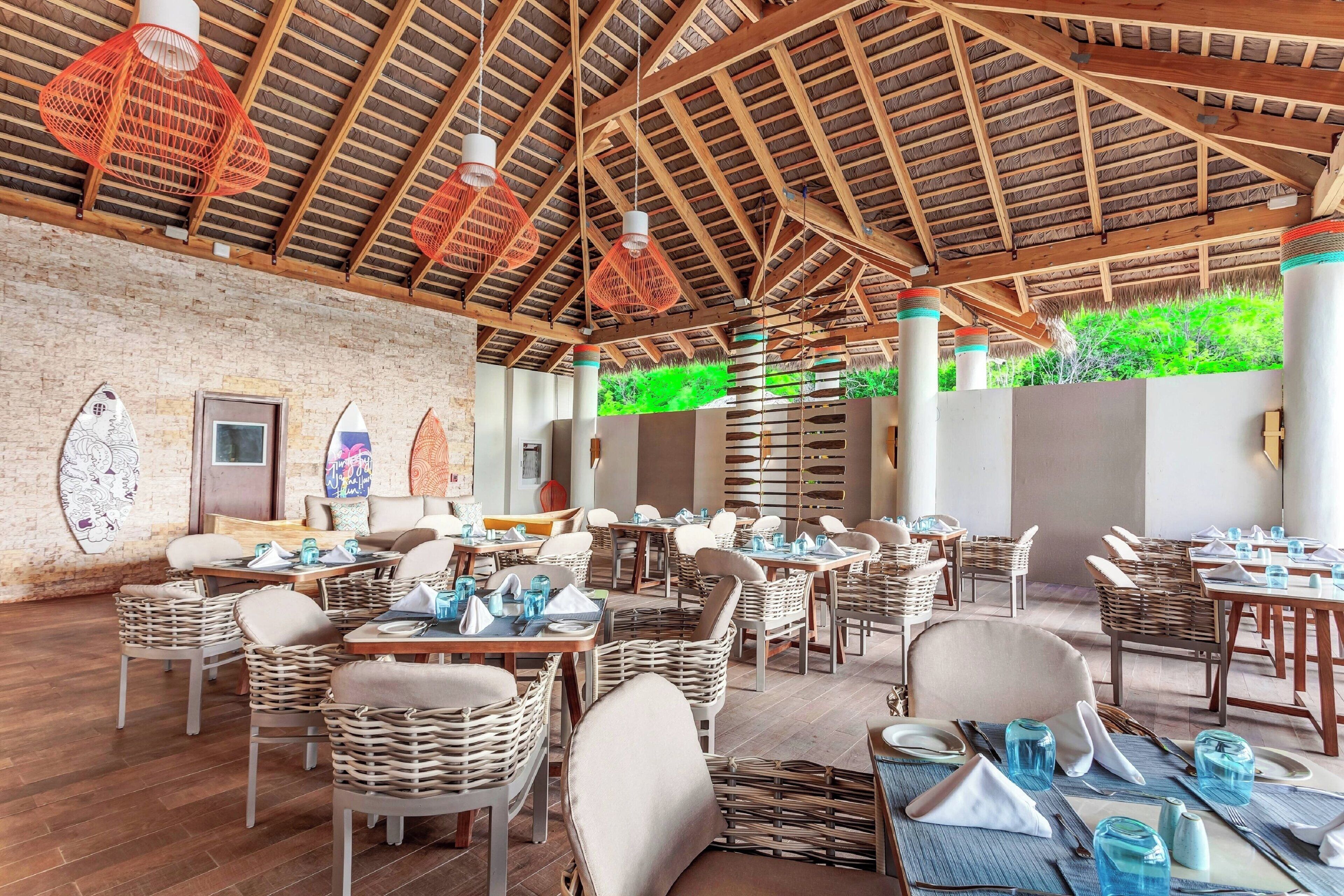 A restaurant with wooden beams, wicker furniture, and a brick wall.