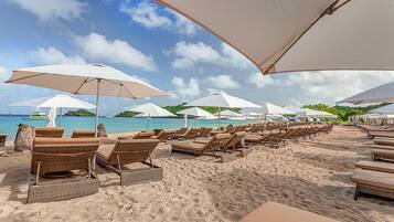 A beach with rows of sun loungers and large umbrellas, a sandy shore, and a view of the sea and distant island.