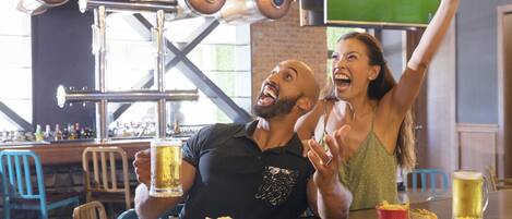 A bar setting with a television displaying a sports game, a man and a woman celebrating, and food and drinks on the table.
