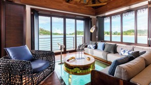 A spacious room with a wooden ceiling, a round coffee table, a sofa, and a wicker chair. Large windows offer a view of the sea and hills. - Royalton Antigua, An Autograph Collection All-Inclusive Resort (St. John's)