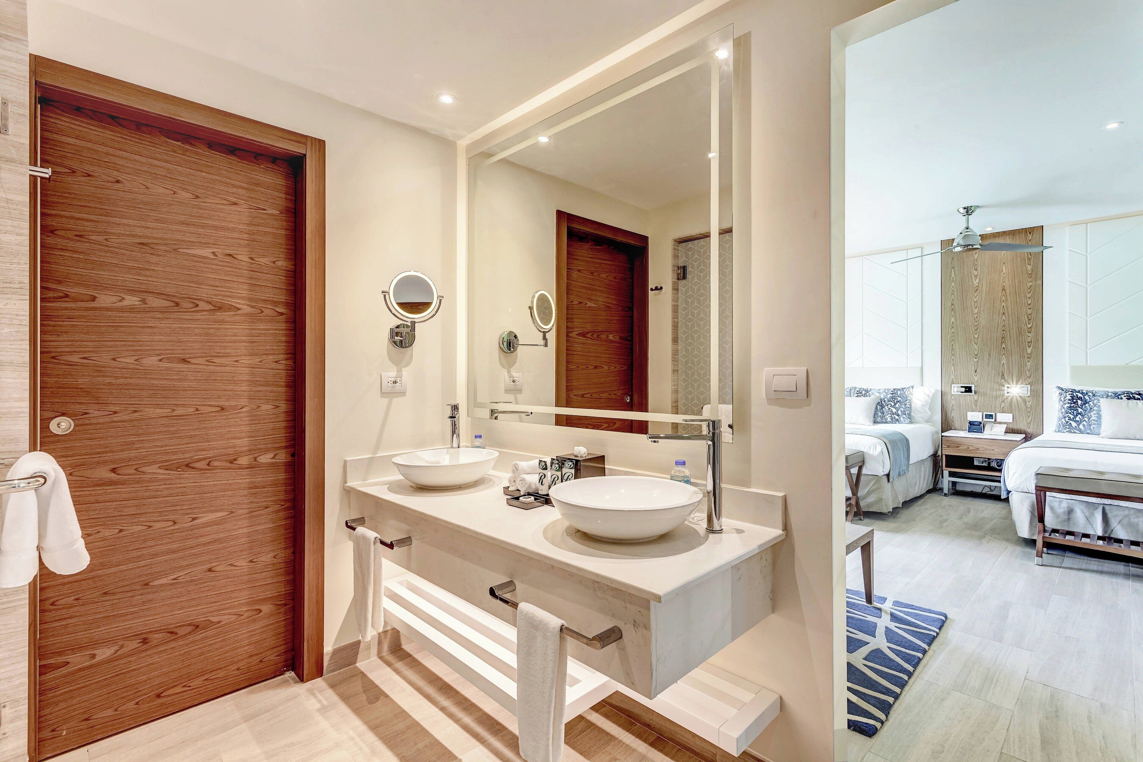 A modern bathroom with two sinks, a large mirror, and a wooden door.