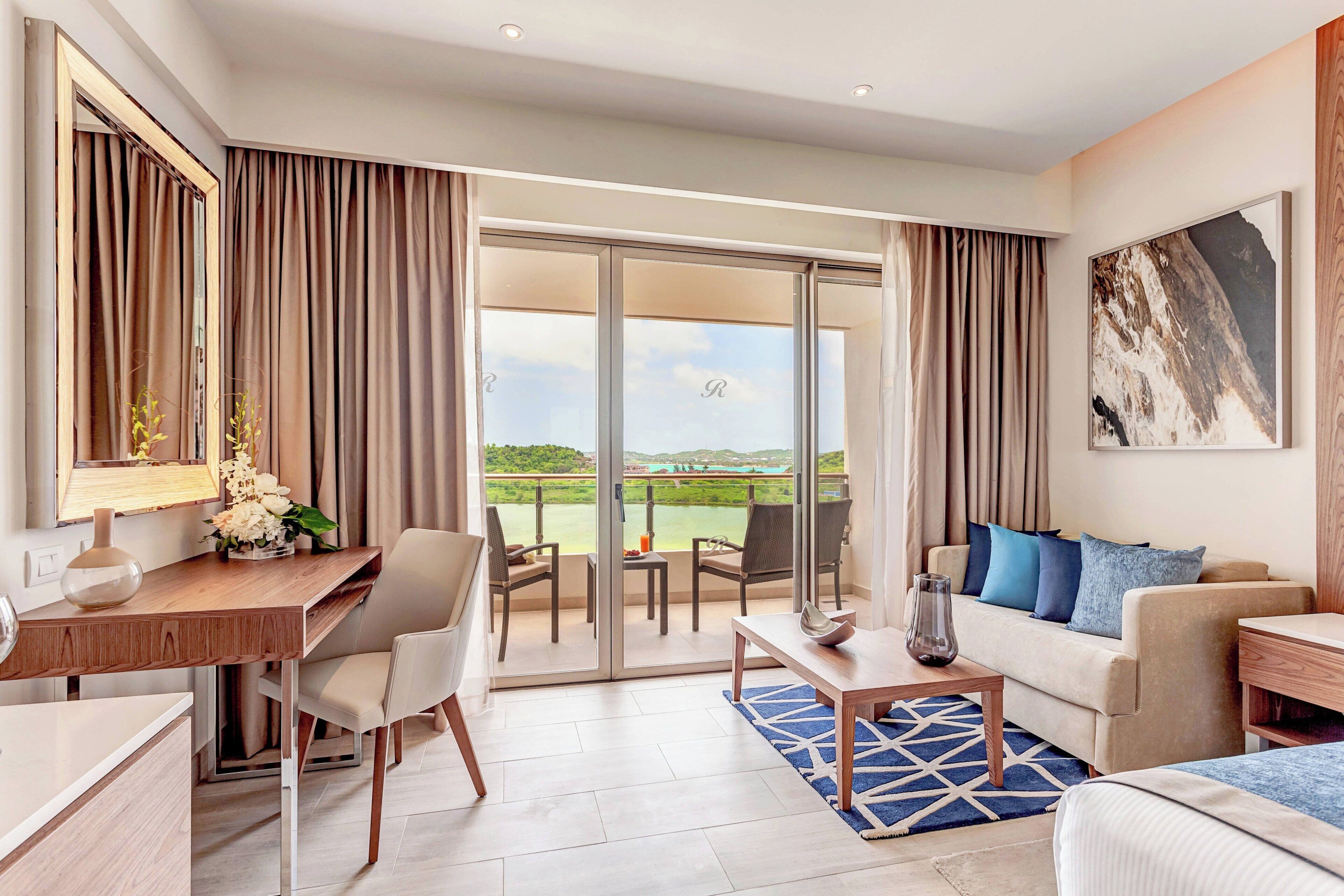 Quarto de hotel moderno com varanda, escrivaninha, sofá e mesa de jantar.